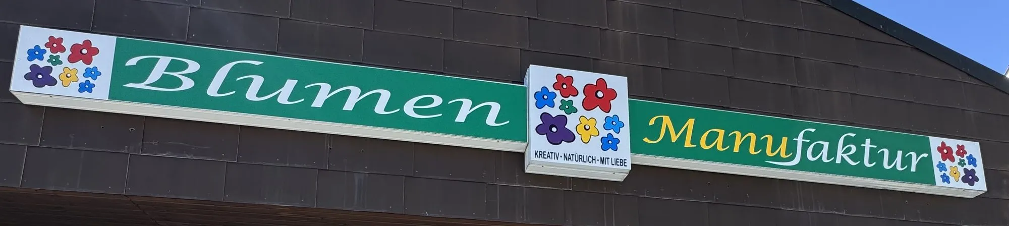 Das Schild „Blumen Manufaktur — kreativ, natürlich, mit Liebe" über dem Laden