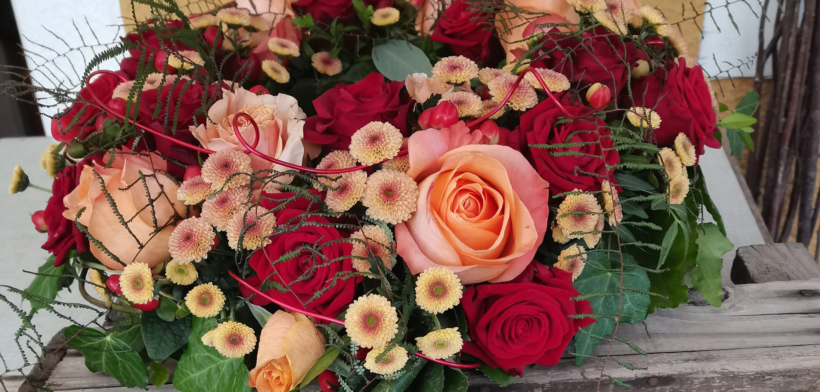 Dicht gestecktes Werkstück aus roten und lachsfarbenen Rosen mit gelben Blüten